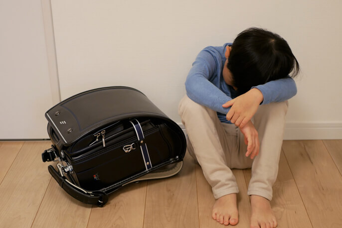 ランドセルを床におき、体操座りをする男の子