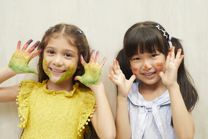 両手を顔の横で広げ笑う外国人と日本人の女の子