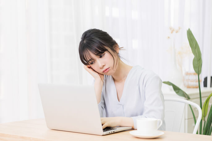 パソコンを見ながら頬杖をつき悩ましげな表情の女性