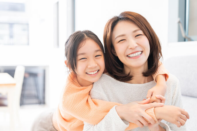 母の方に腕を回して抱きつきながら笑う女の子