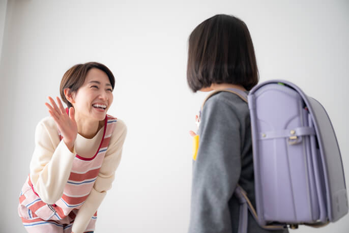 ランドセルを背負った女の子と笑いかけるエプロン姿の母