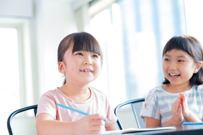 筆記用具を持つ女の子とその隣で笑う女の子