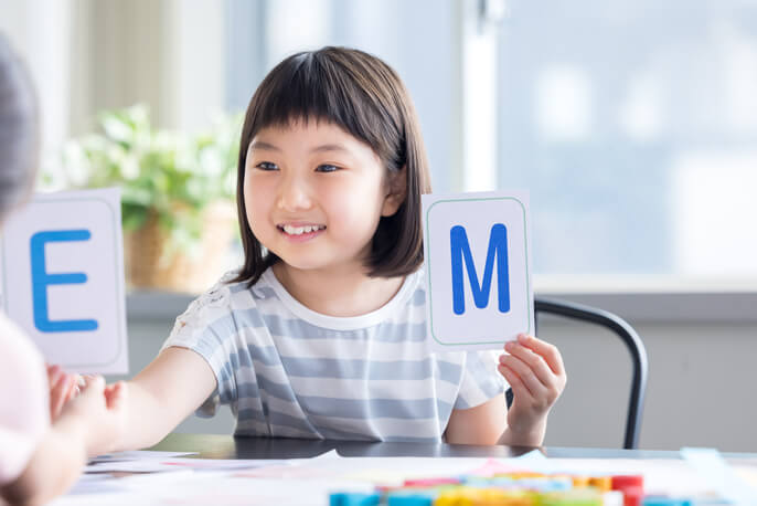 アルファベットのカードをもって笑う女の子